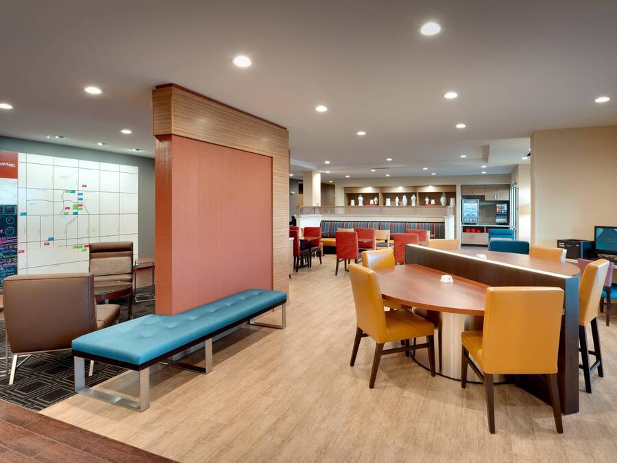 A modern hotel lobby with a long wooden table, multiple seating areas, and a map on the wall.