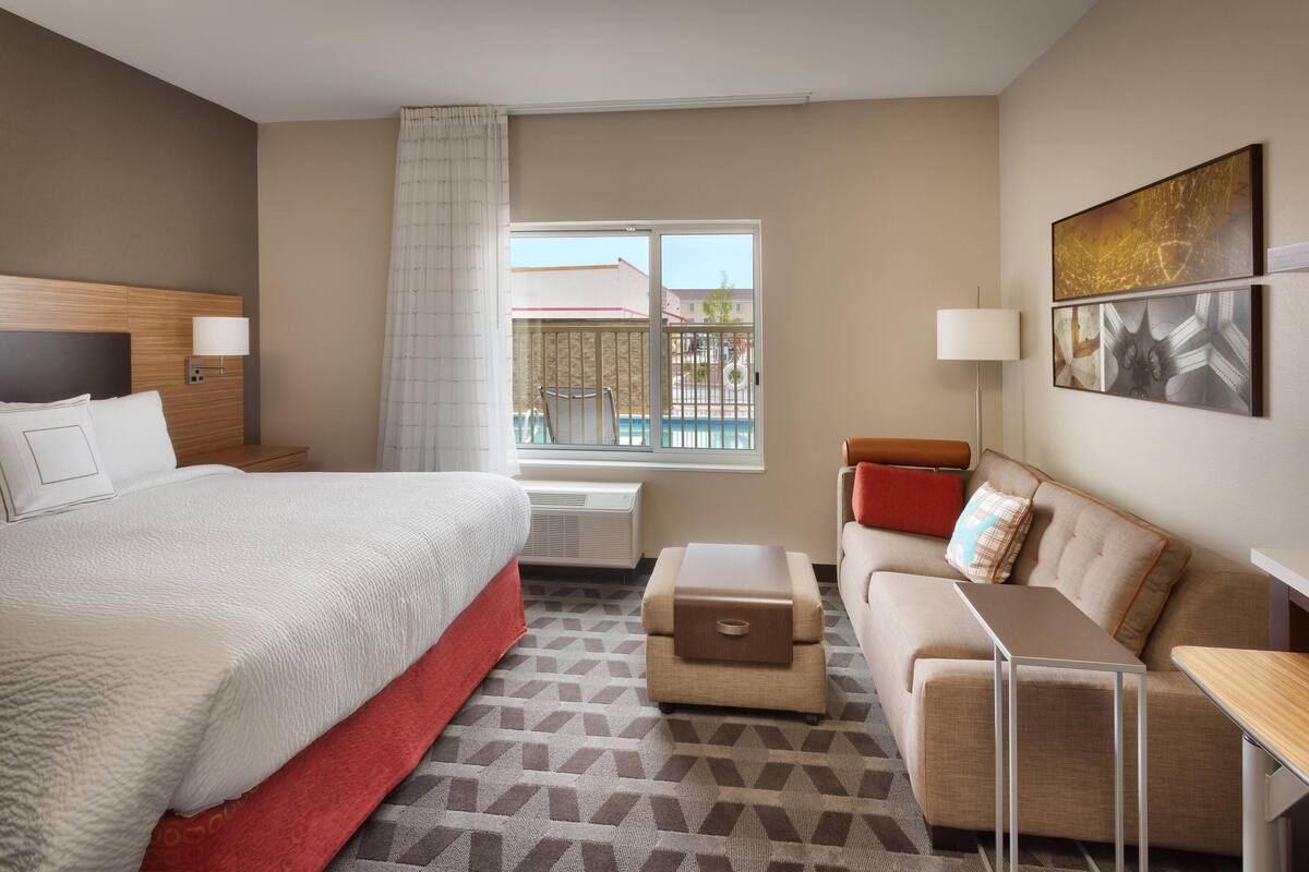 Une chambre d’hôtel avec un lit, un canapé, une petite table, une fenêtre donnant sur une piscine et un tableau au mur.