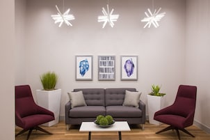 Una sala de estar moderna con un sofá gris, dos sillones rojos, una mesa de centro blanca y tres obras de arte enmarcadas en la pared.