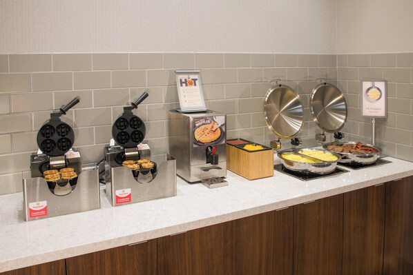 A breakfast buffet with waffle irons, a waffle maker, and various food items like eggs and meats. - Fairfield by Marriott Inn & Suites Dayton Downtown (Dayton)