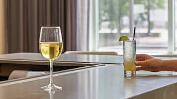 A bar area with a glass of white wine and a tall glass of a yellow beverage with a lime wedge and straw.