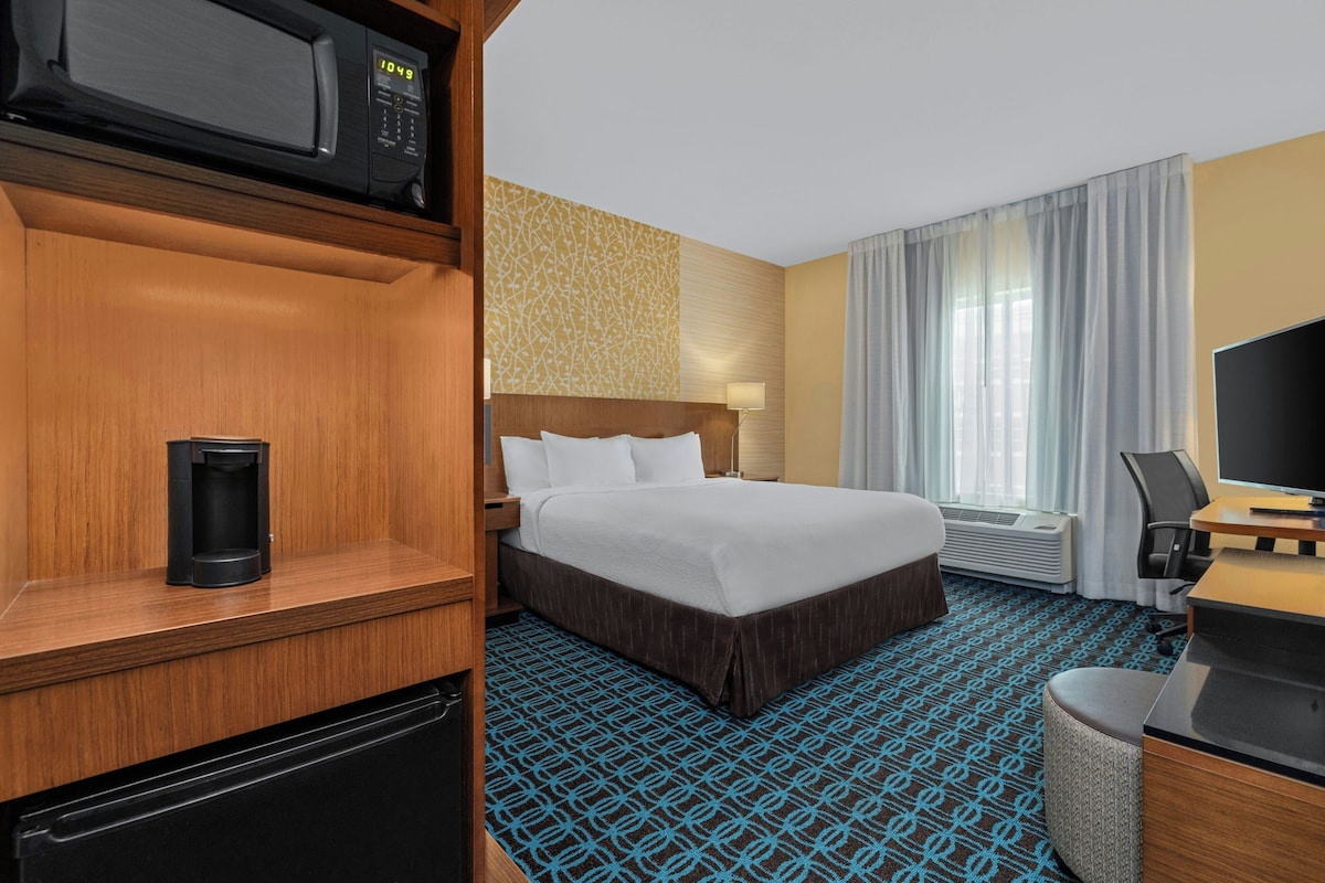 Een hotelkamer met een bed, een bureau, een televisie, een koffiezetapparaat en een magnetron.