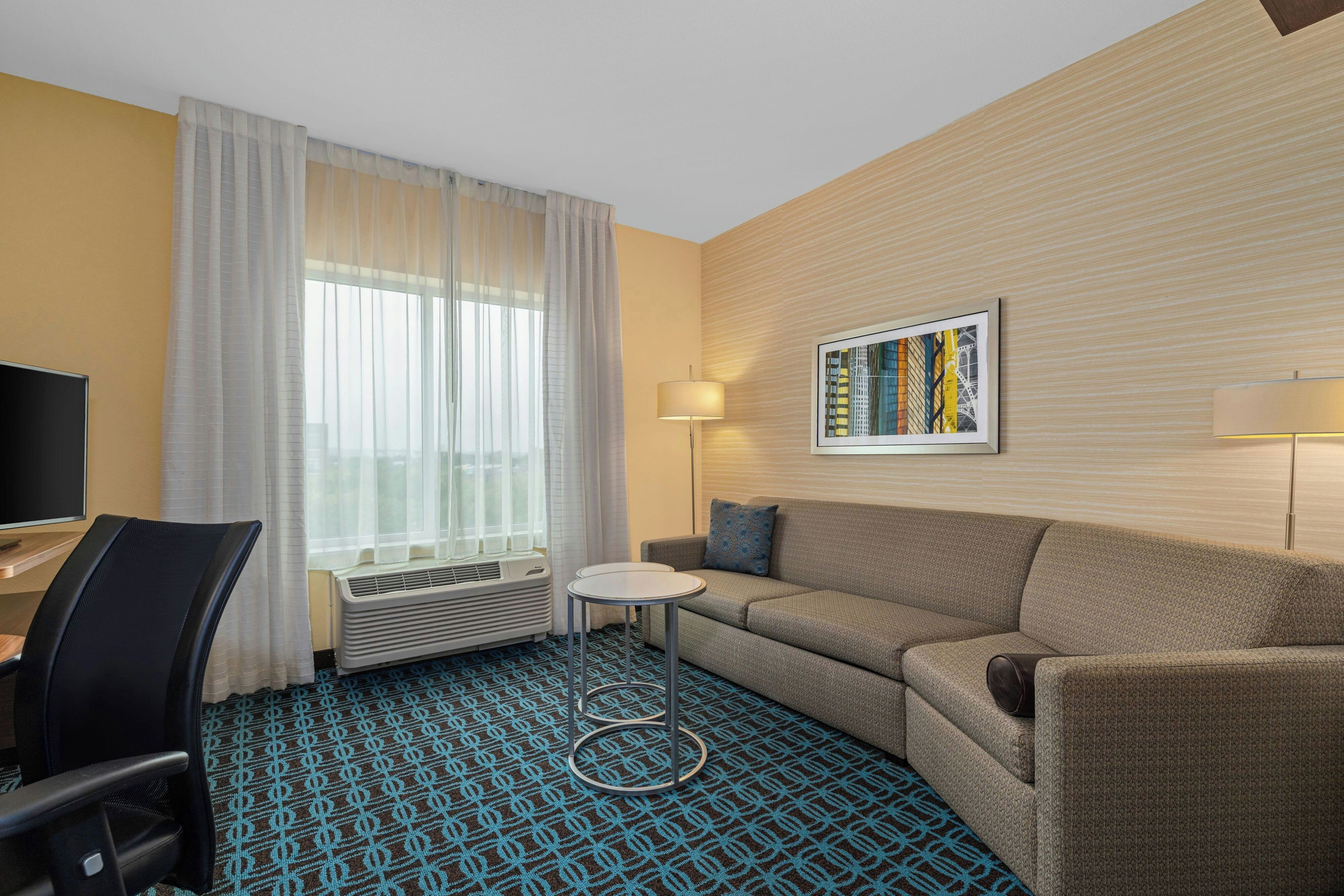 Habitació d'hotel amb un sofà, una taula petita, una televisió i una finestra amb cortines.
