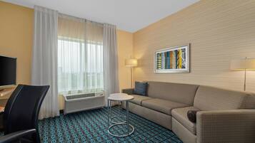 Habitació d'hotel amb un sofà, una taula petita, una televisió i una finestra amb cortines.
