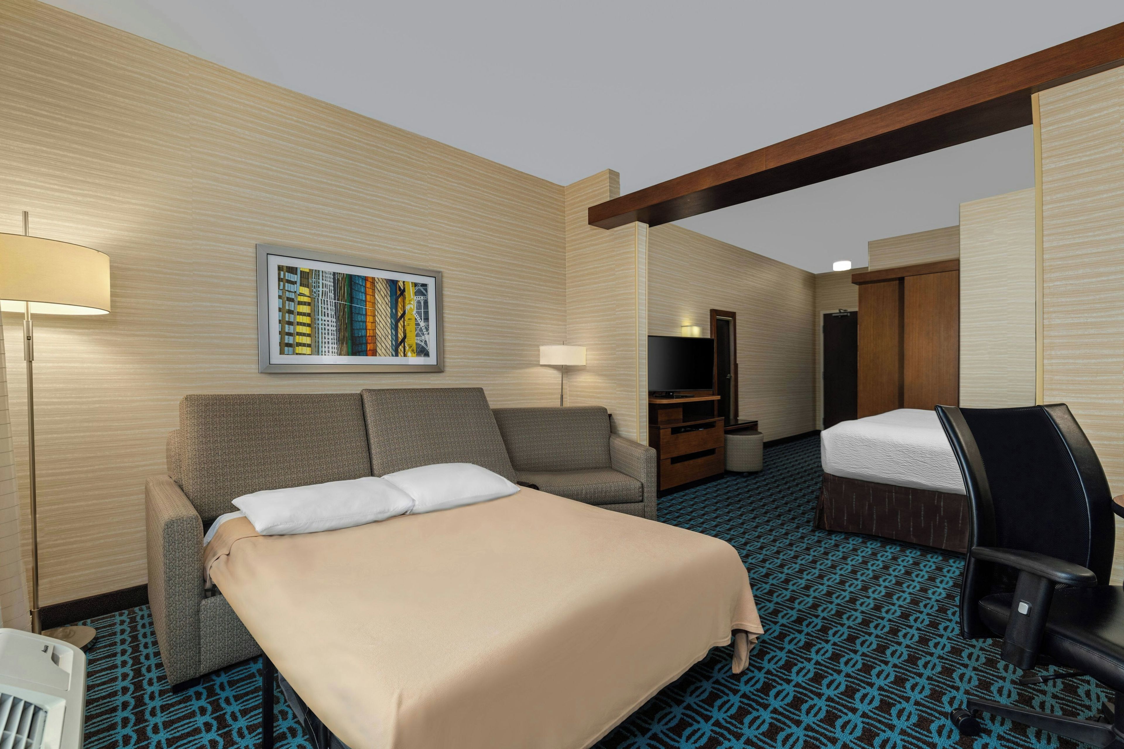 Een hotelkamer met een bed, een bank, een bureau, een televisie en een schilderij aan de muur.