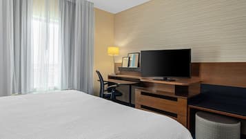 Habitació d'hotel amb un llit gran, una taula de treball, un televisor, una cadira i una làmpada.