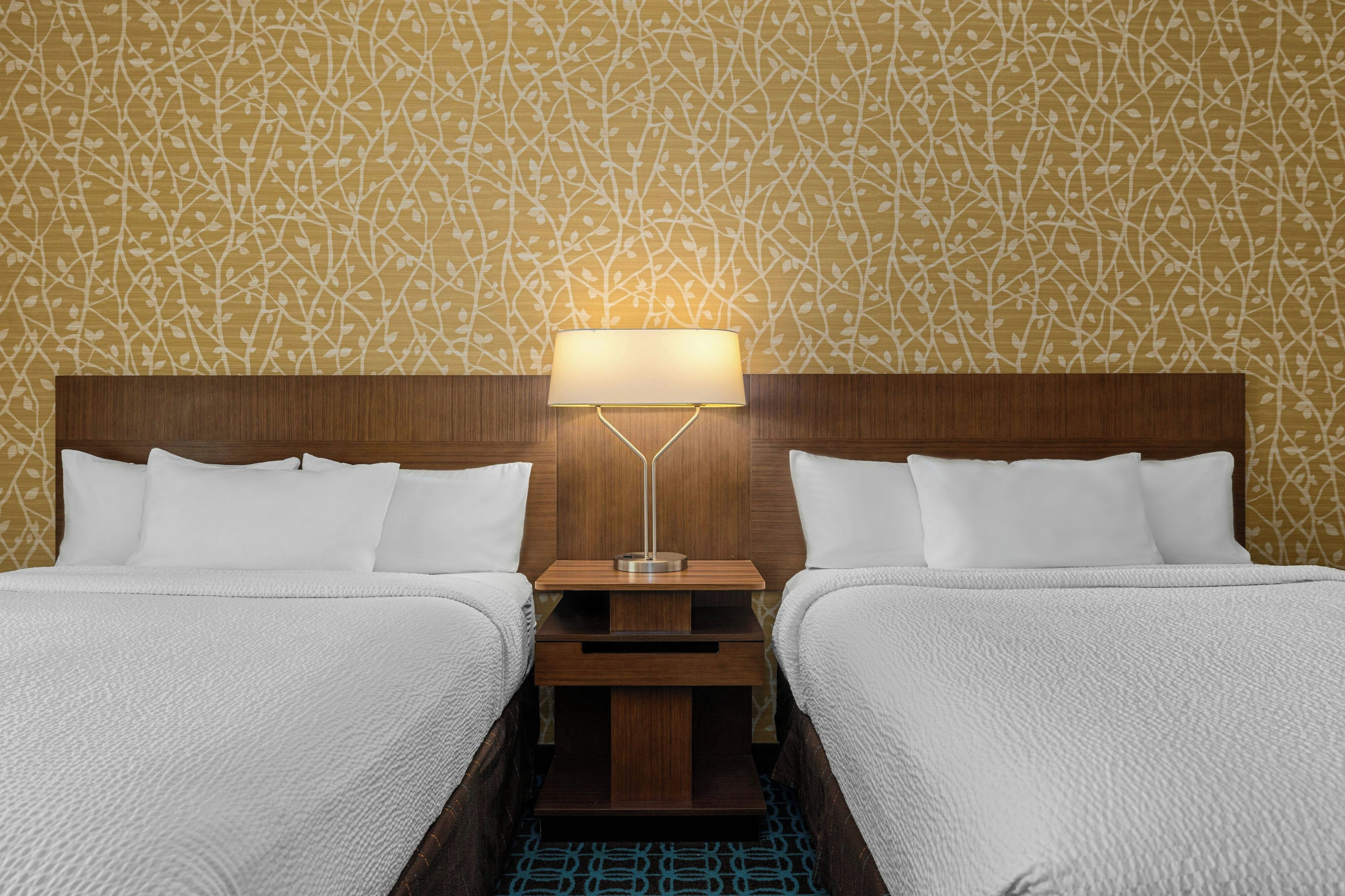 A double bed with white bedding, a nightstand with a lamp, and a patterned wall.