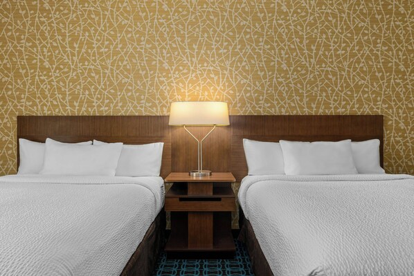 A double bed with white bedding, a nightstand with a lamp, and a patterned wall.