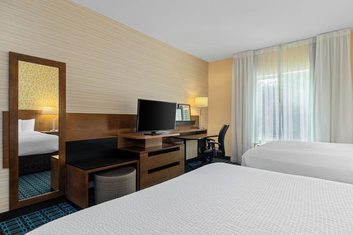 Een hotelkamer met twee bedden, een bureau met een televisie, een stoel en een groot raam met gordijnen.