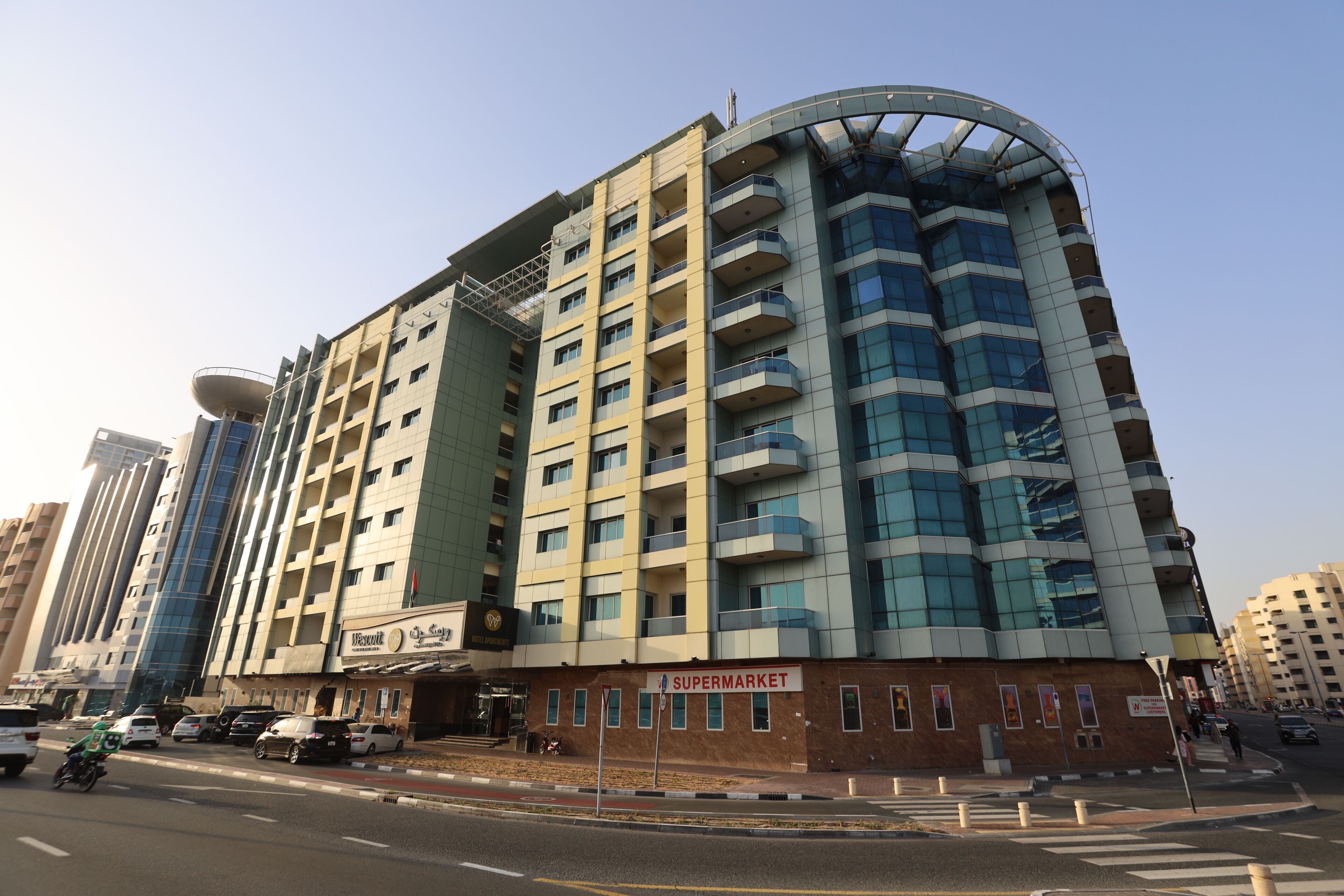 A multi-story building with a supermarket on the ground floor, a curved glass facade, and a rooftop structure.