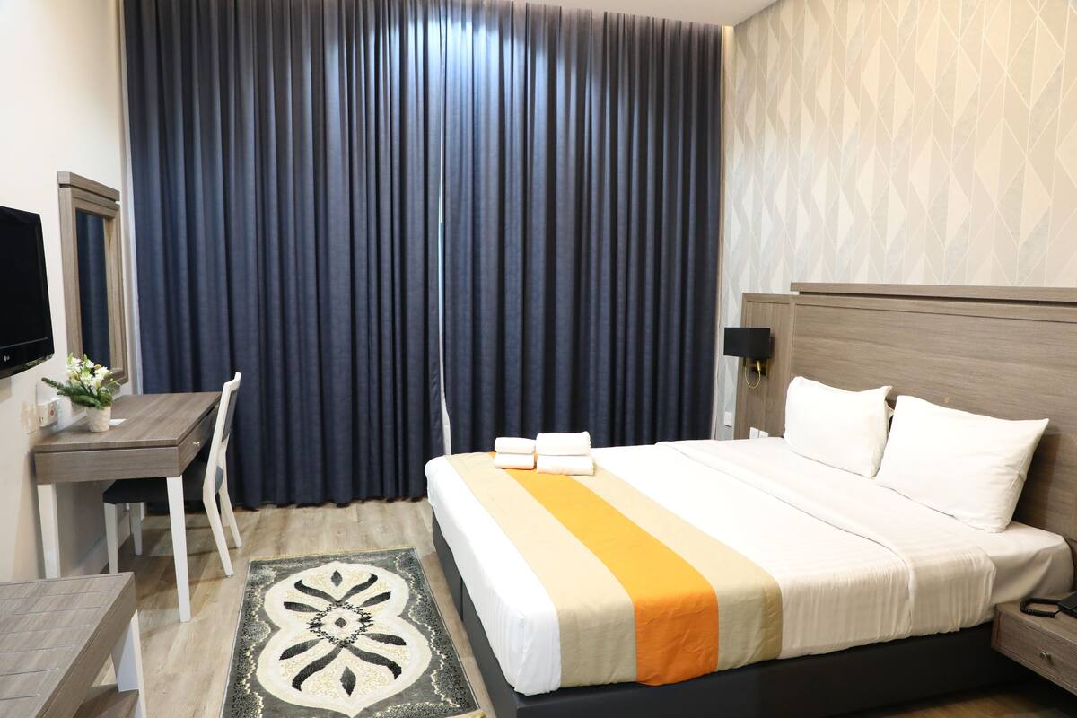 A hotel room with a bed, a desk, a chair, a TV, and a large window with curtains.