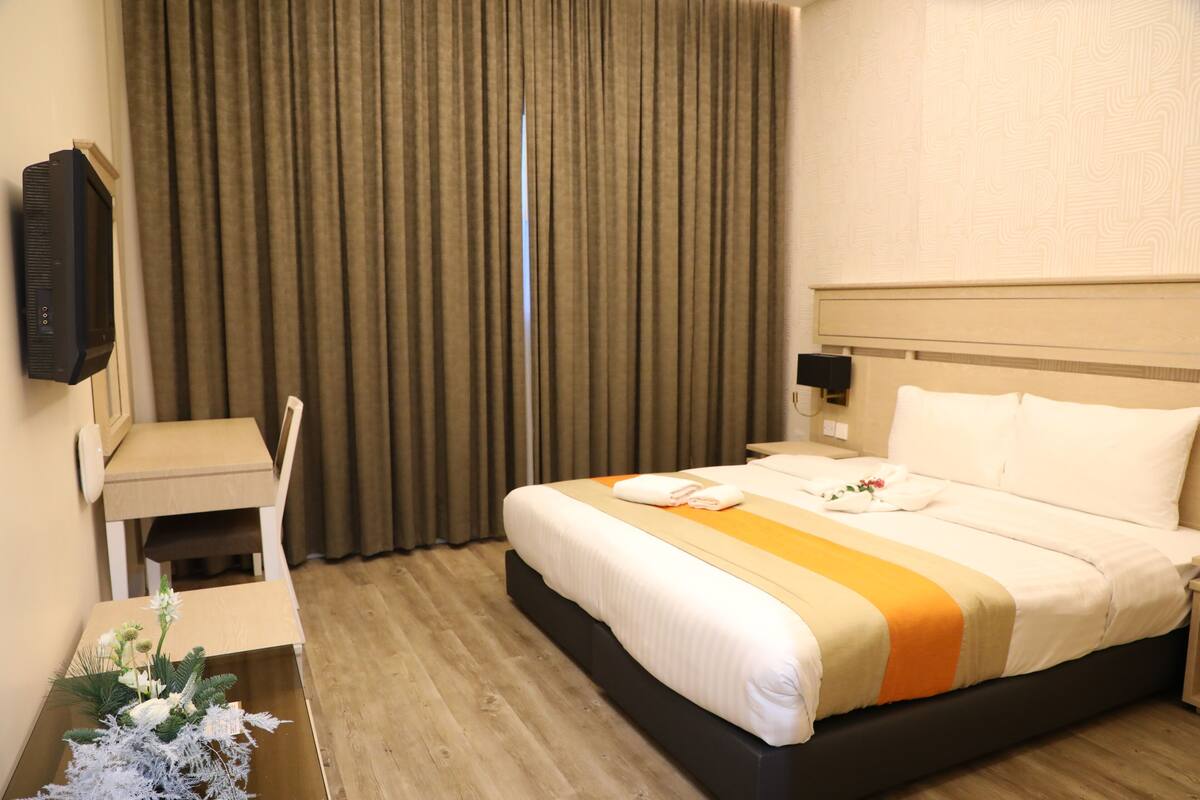 A hotel room with a bed, a desk, a chair, a TV, and a curtain.