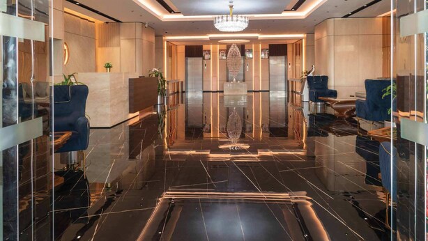 A modern lobby with a chandelier, marble flooring, and blue upholstered chairs. - Wescott Plaza Hotel Apartment (Dubai)