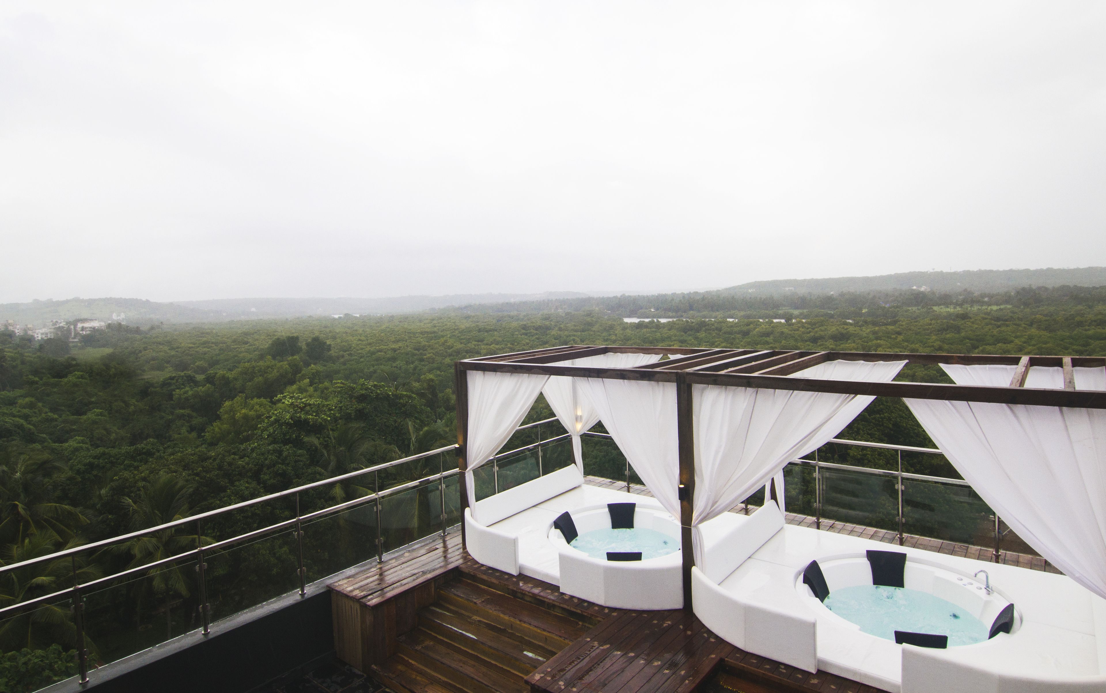 Terraza en la azotea con dos jacuzzis y una cubierta de madera, con vistas a un paisaje verde y exuberante.
