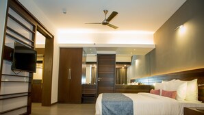 A modern hotel room with a large bed, a flat-screen TV, a ceiling fan, and a wooden wardrobe. - SinQ Prive (Candolim)