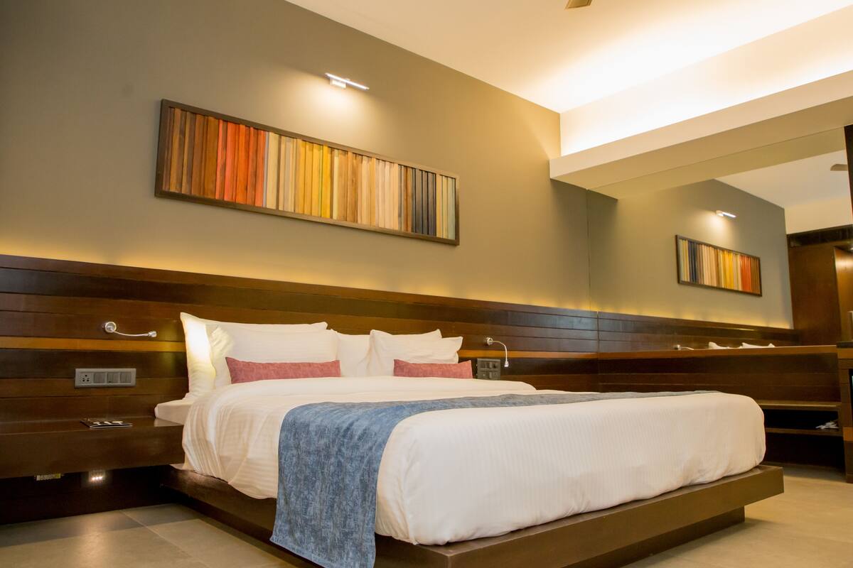 Une chambre d’hôtel moderne avec un grand lit, une tête de lit en bois et une œuvre d’art accrochée au mur.