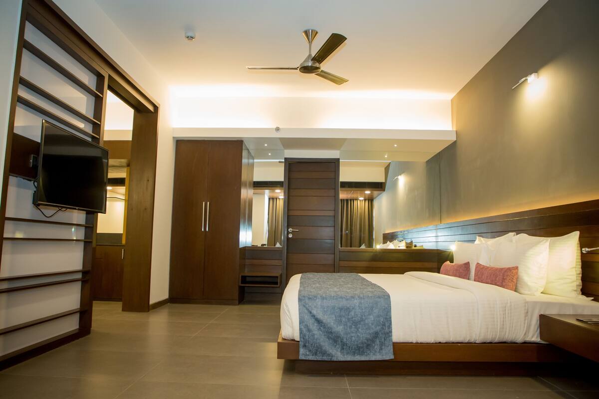 Une chambre d’hôtel moderne équipée d’un lit, d’un téléviseur à écran plat, d’un ventilateur de plafond et d’une armoire en bois.