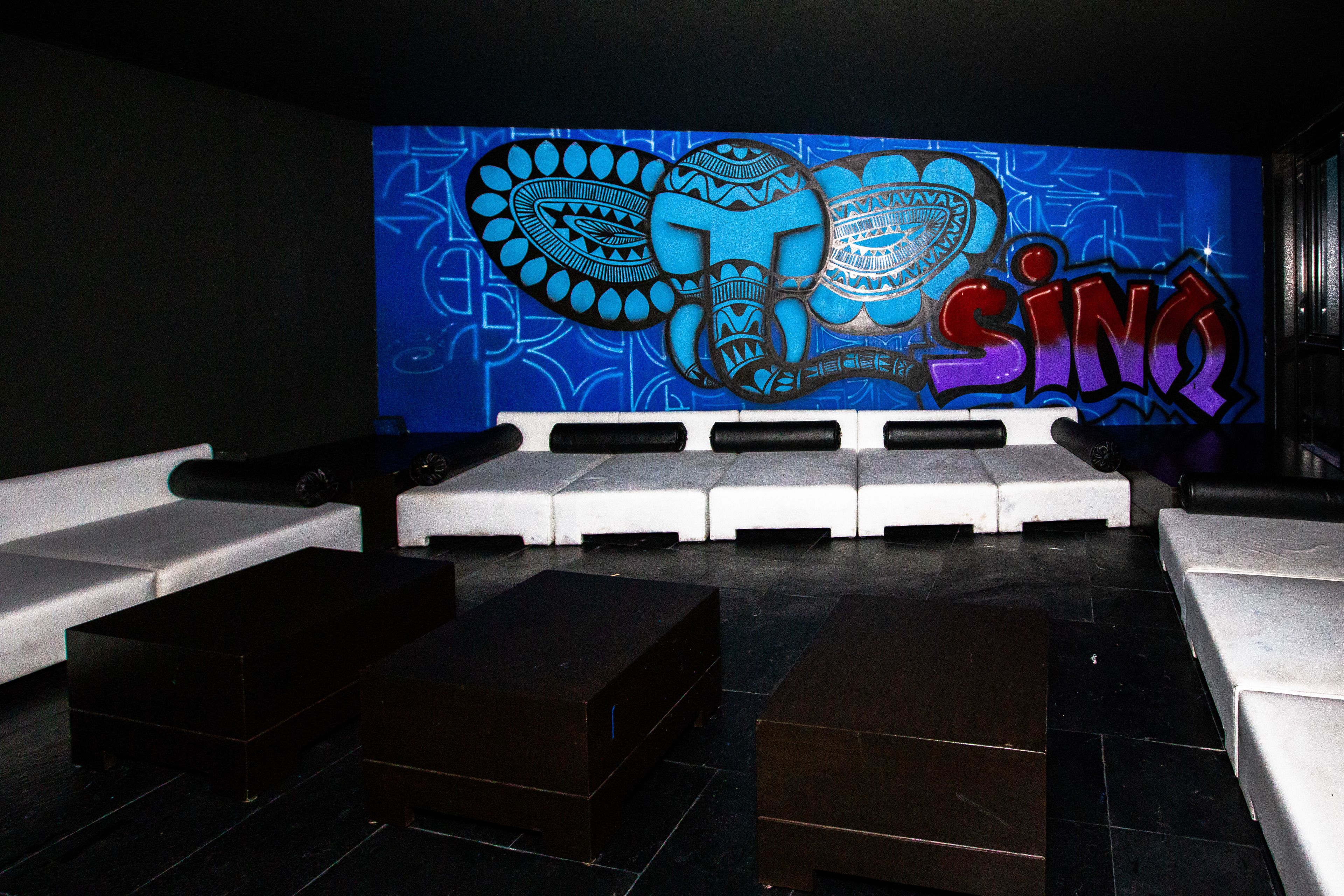 Espaço lounge moderno com um grande mural na parede, sofás brancos e piso estampado.