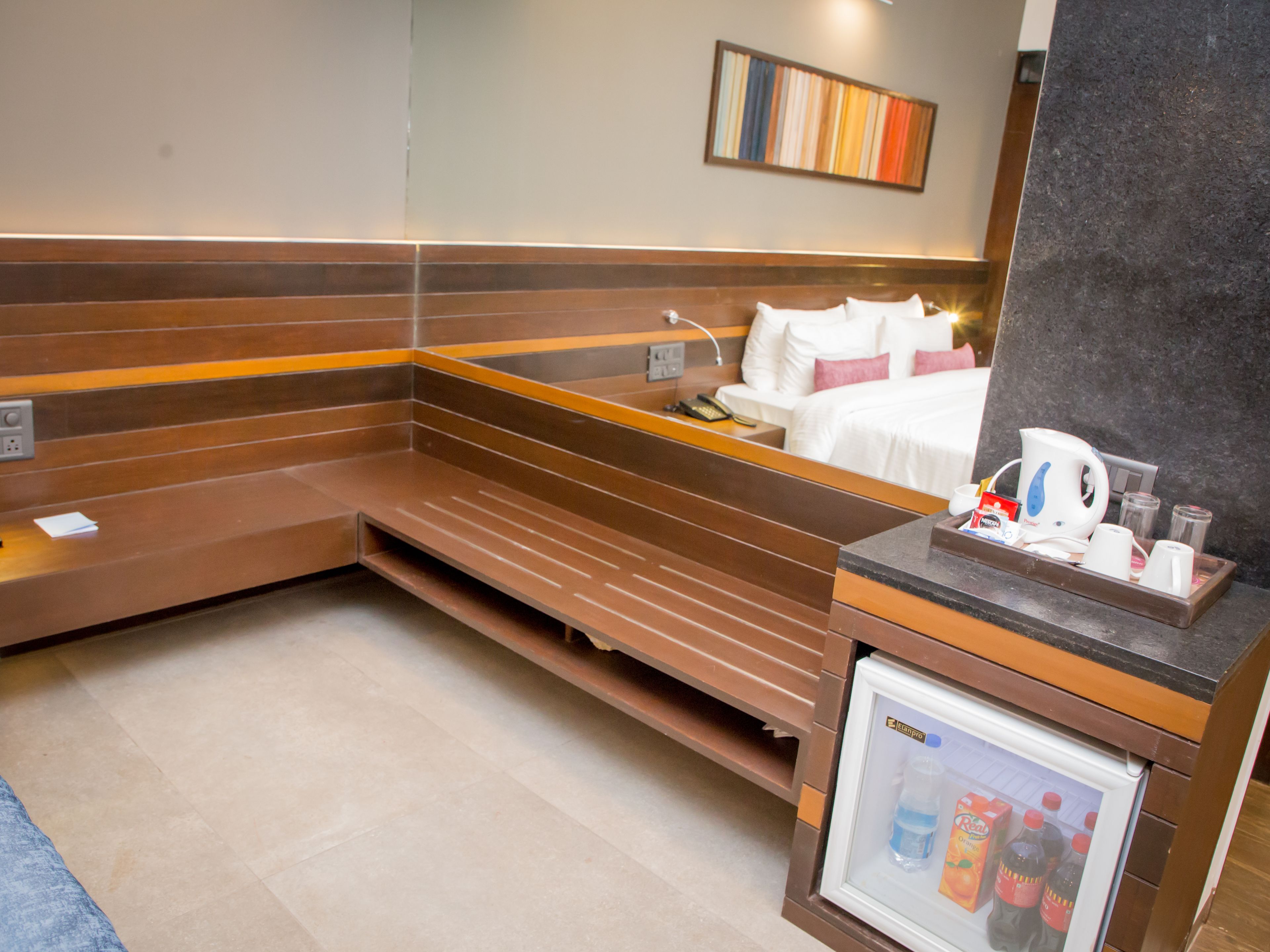 Habitación de hotel con cama, un pequeño rincón de estar, minibar y una obra de arte colgada en la pared.
