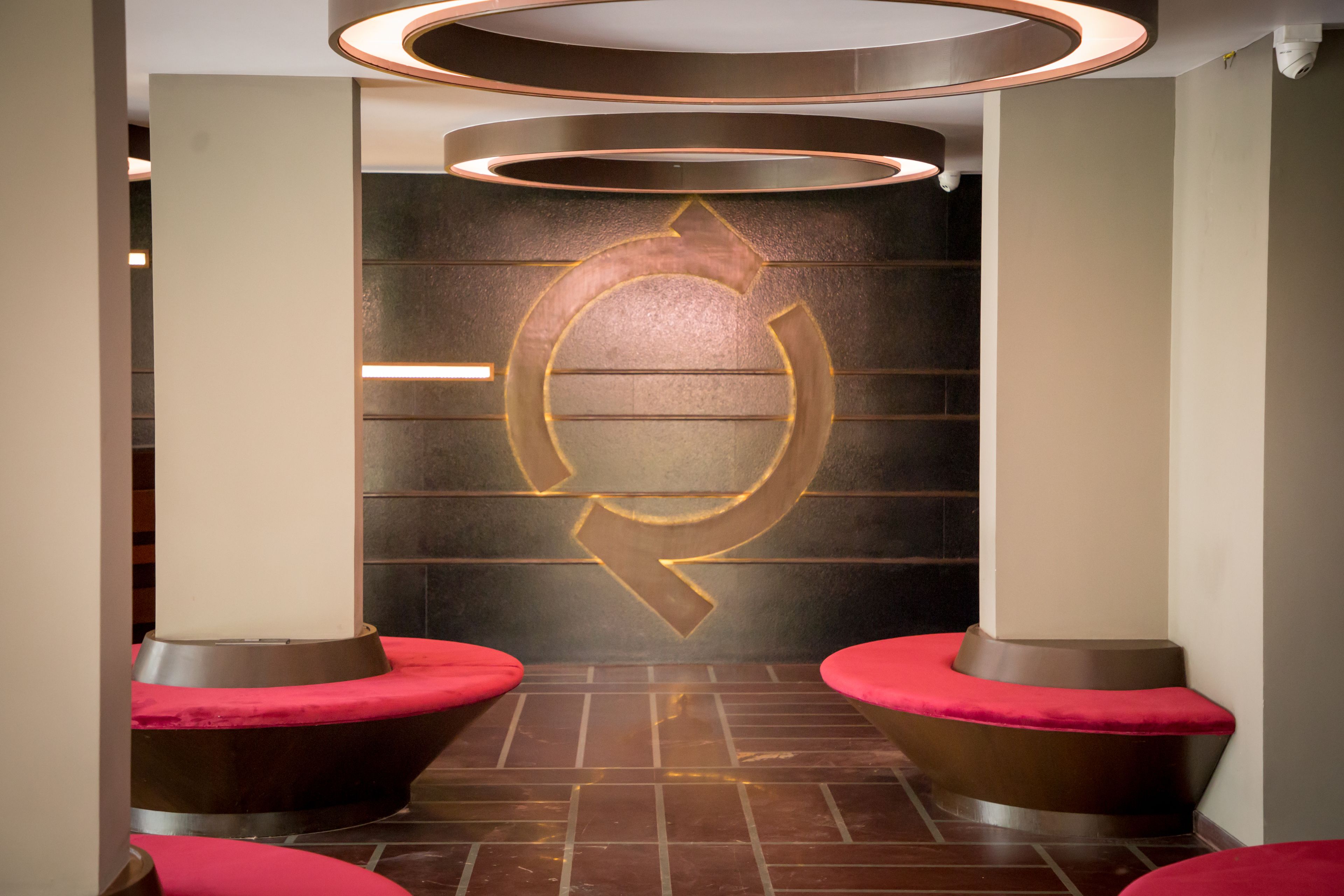 A modern interior with a circular logo on the wall, two red cushioned seating areas, and a patterned floor.