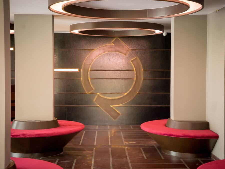 A modern interior with a circular logo on the wall, two red cushioned seating areas, and a patterned floor.