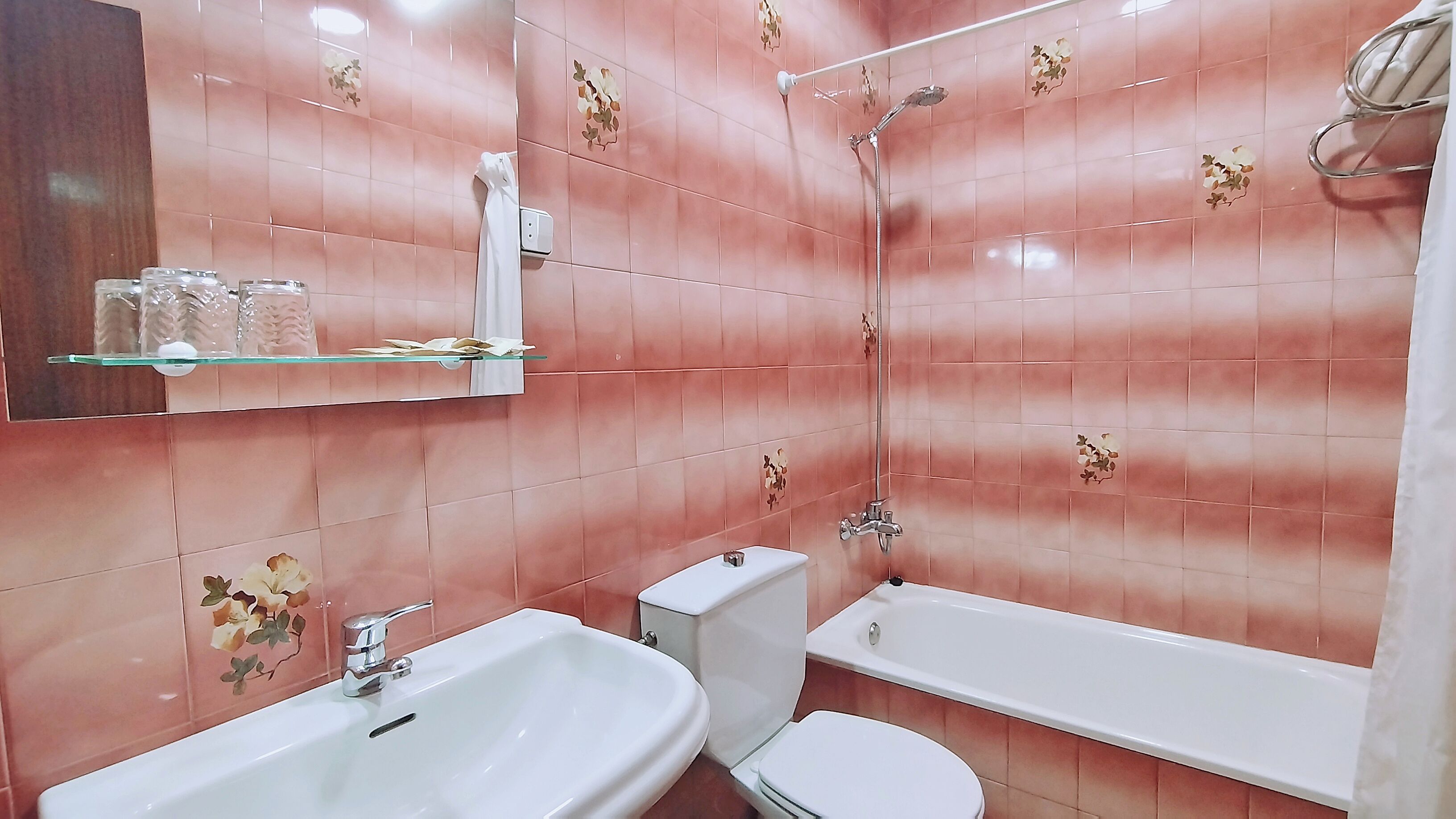A bathroom with pink tiles, a white sink, a toilet, and a bathtub.
