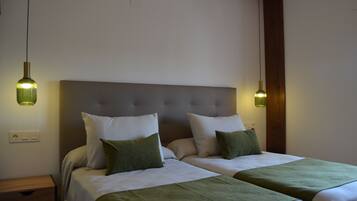 Una cama doble con cabecera gris, dos mesitas de noche y cojines decorativos verdes.