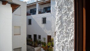 A narrow alleyway with white buildings, balconies, and potted plants.