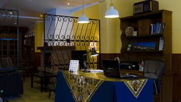 A reception desk with a laptop, a telephone, and a lamp. There is a bookshelf with books and a decorative item.