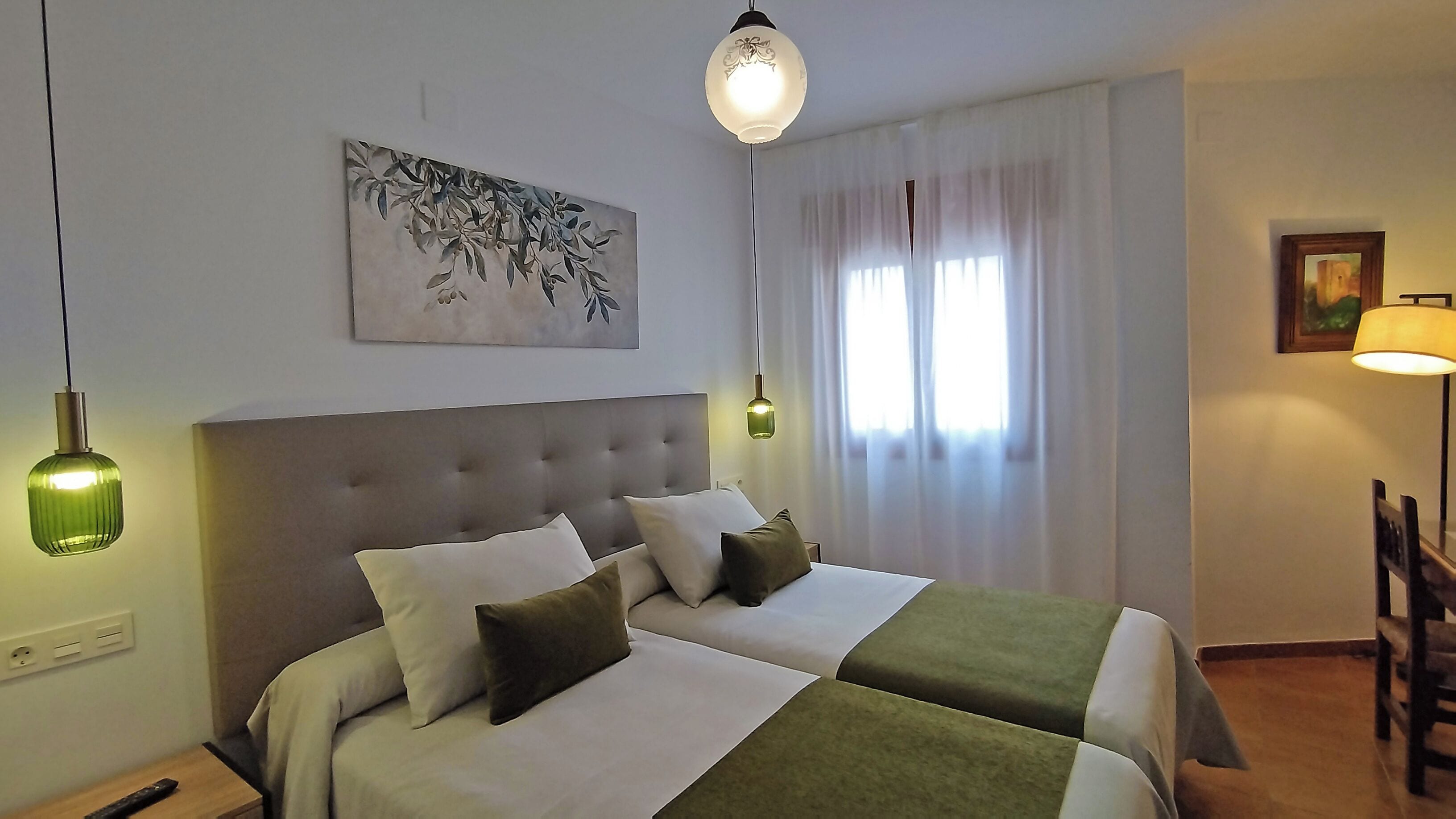 Habitació d'hotel amb un llit gran, dues taules de nit, un quadre a la paret i una finestra amb cortines.