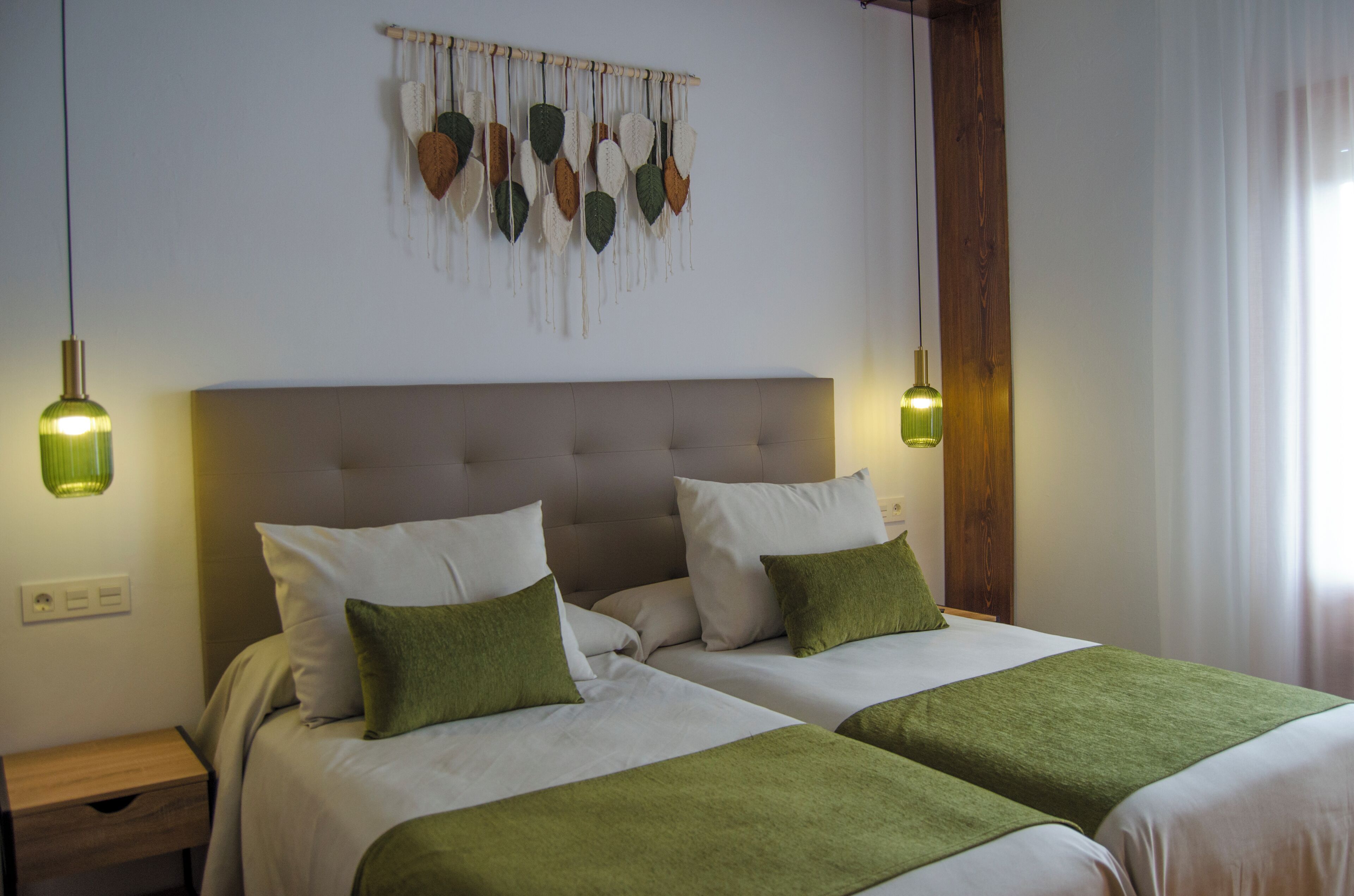 A hotel room with two beds, a wooden headboard, a wall hanging, and two bedside lamps.