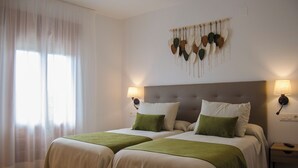 A hotel room with two beds, a large window with sheer curtains, a wall-mounted decorative piece, and bedside lamps.