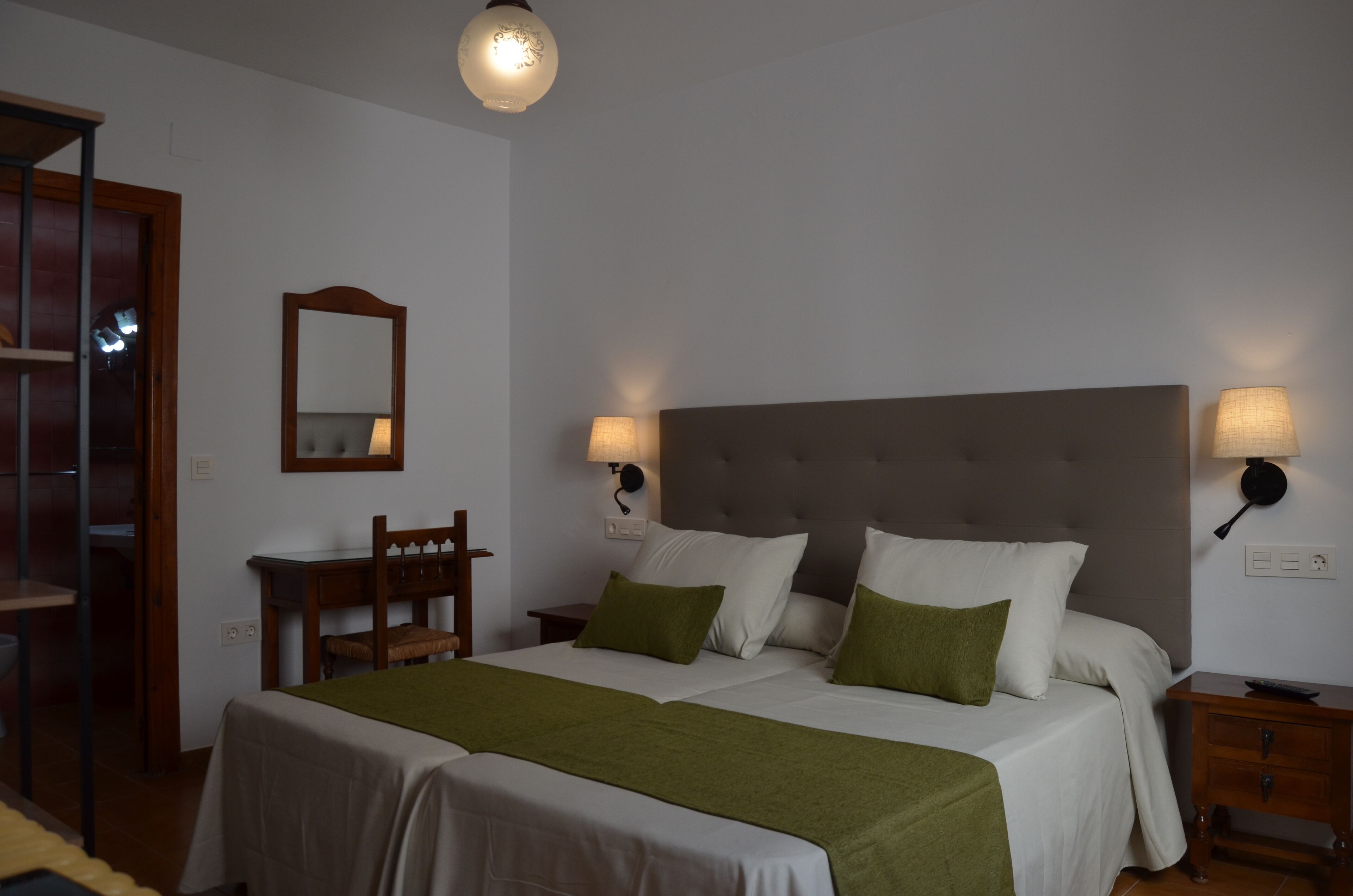Un letto matrimoniale con una coperta verde, due abat-jour, uno specchio e un comodino in legno.