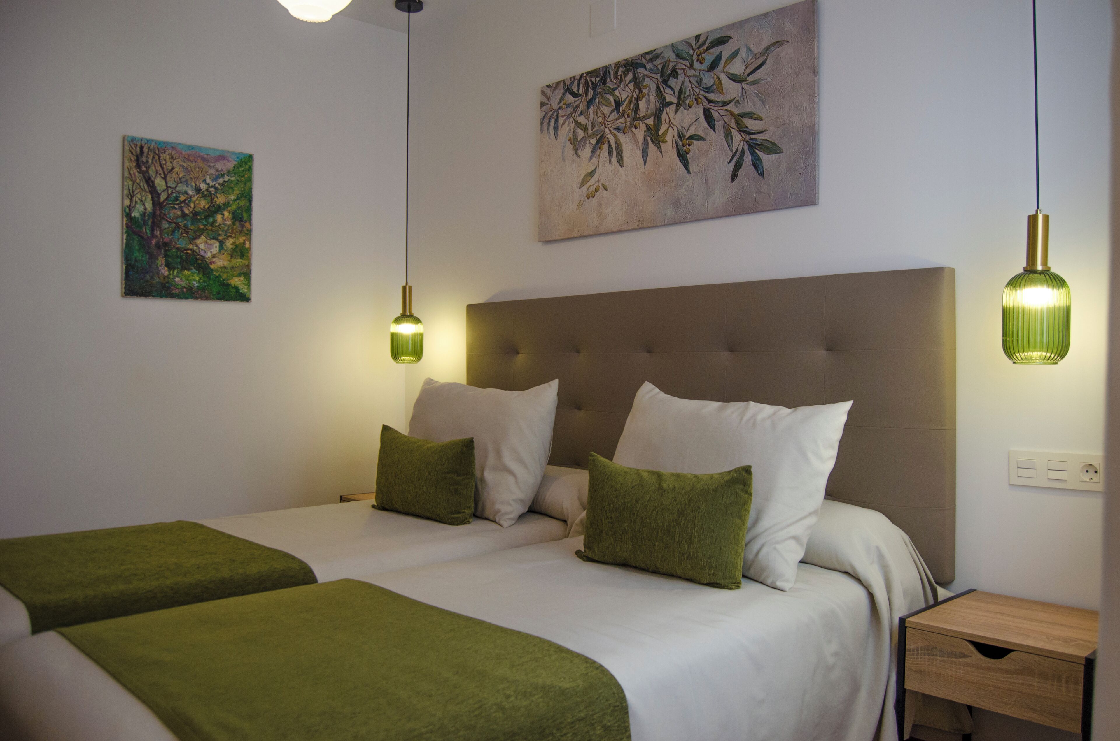 A bedroom with two beds, a headboard, bedside tables, and wall art.