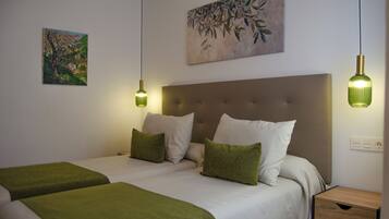 A bedroom with two beds, a headboard, bedside tables, and wall art.