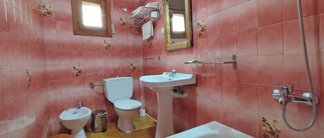 A bathroom with pink tiles, a toilet, bidet, sink, bathtub, and a shower.
