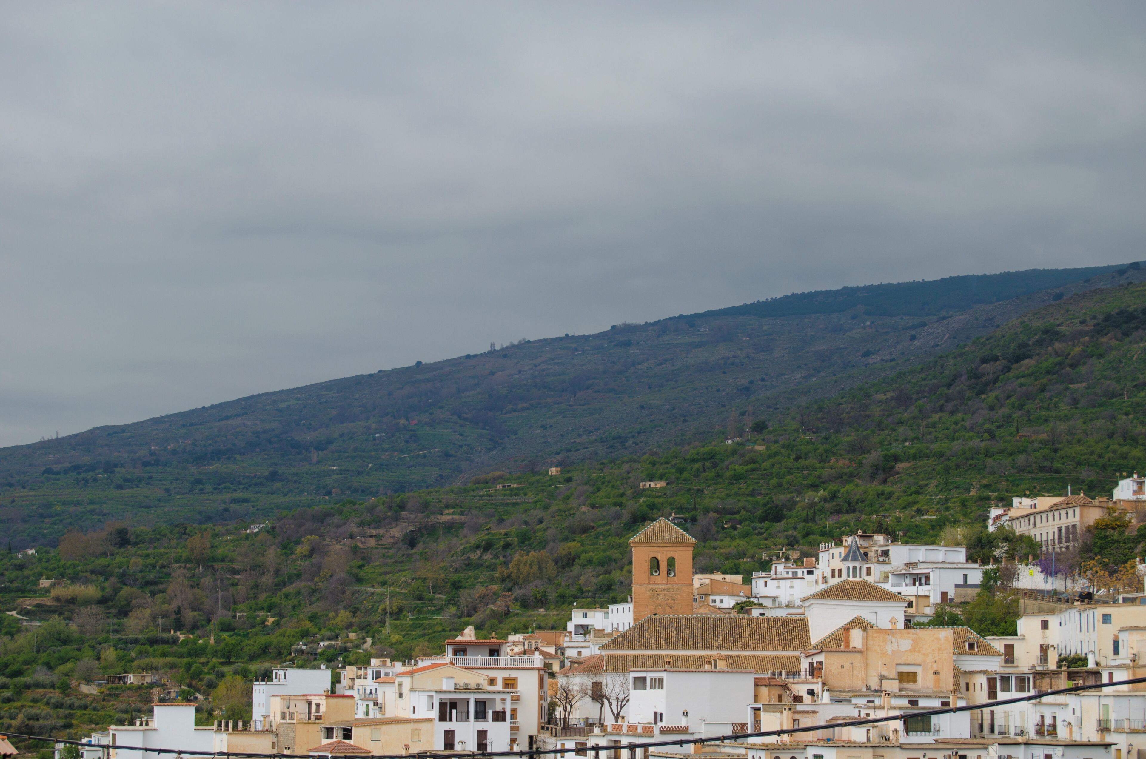 A hillside town with buildings, a prominent tower, and a hilly backdrop.