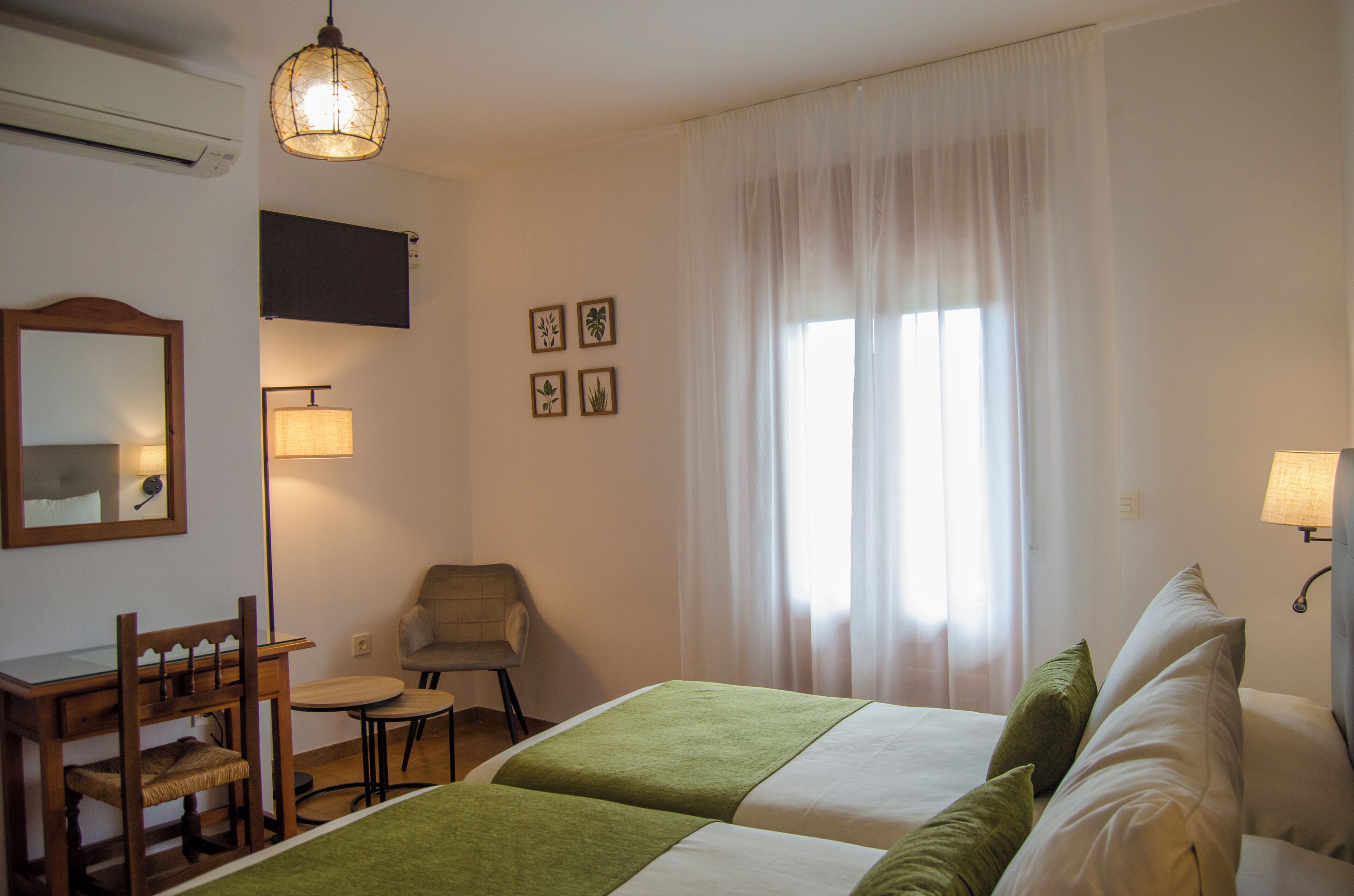 Una habitación de hotel con cama, escritorio, silla, lámpara y ventana con cortinas.