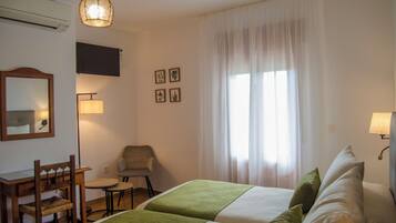 Una habitación de hotel con cama, escritorio, silla, lámpara y ventana con cortinas.