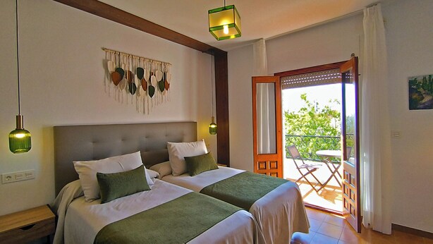 A bedroom with two beds, a balcony with a table and chairs, and a decorative wall hanging.