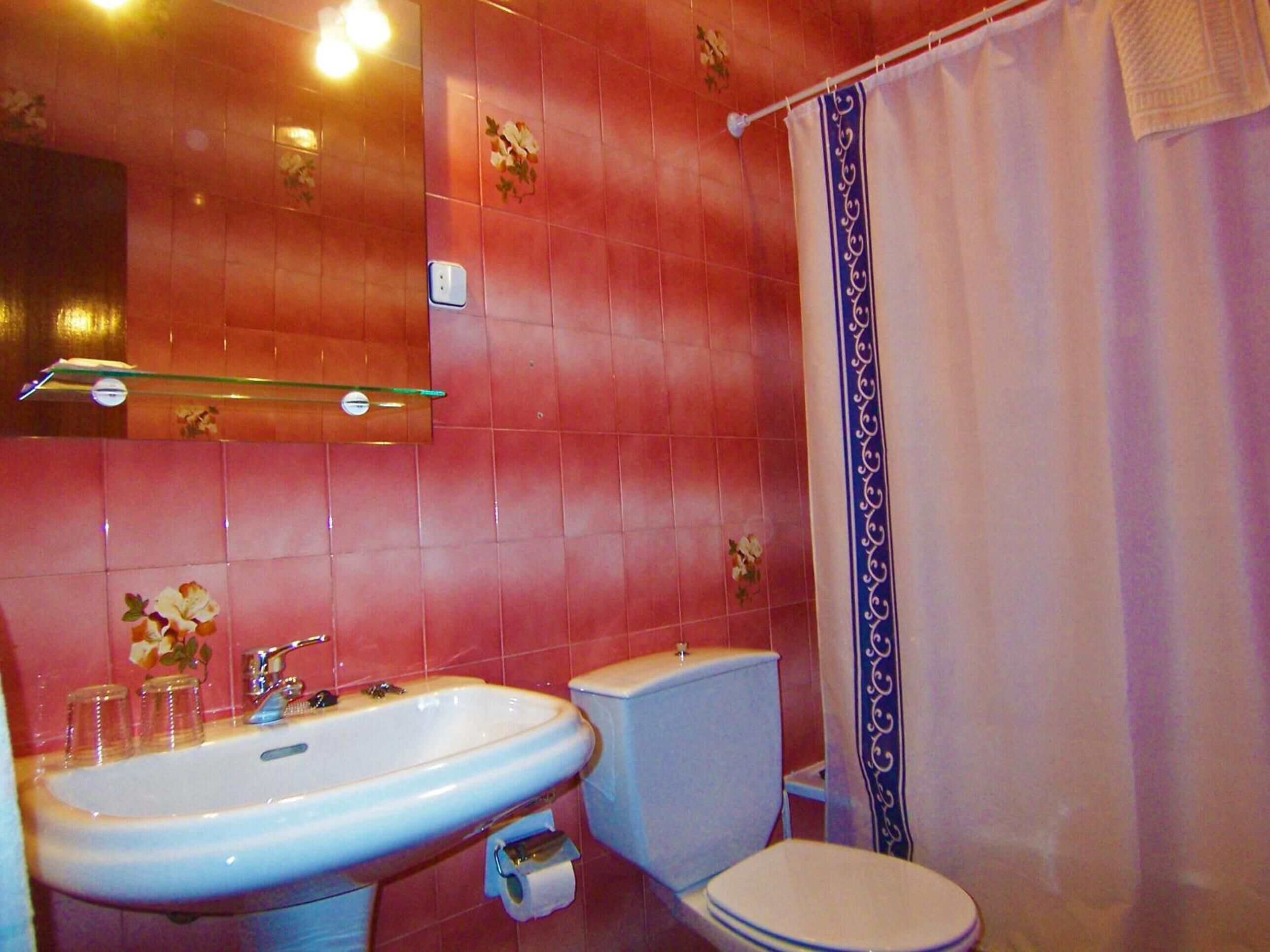 A bathroom with pink tiled walls, a white sink, a toilet, and a shower curtain.