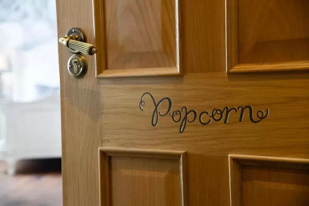 A wooden door with a brass handle and a keyhole. The word "Popcorn" is written on the door in cursive.