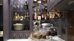 A kitchen with a glass display case containing various bottles and a glass display case with desserts. - Padstow Townhouse (Padstow)