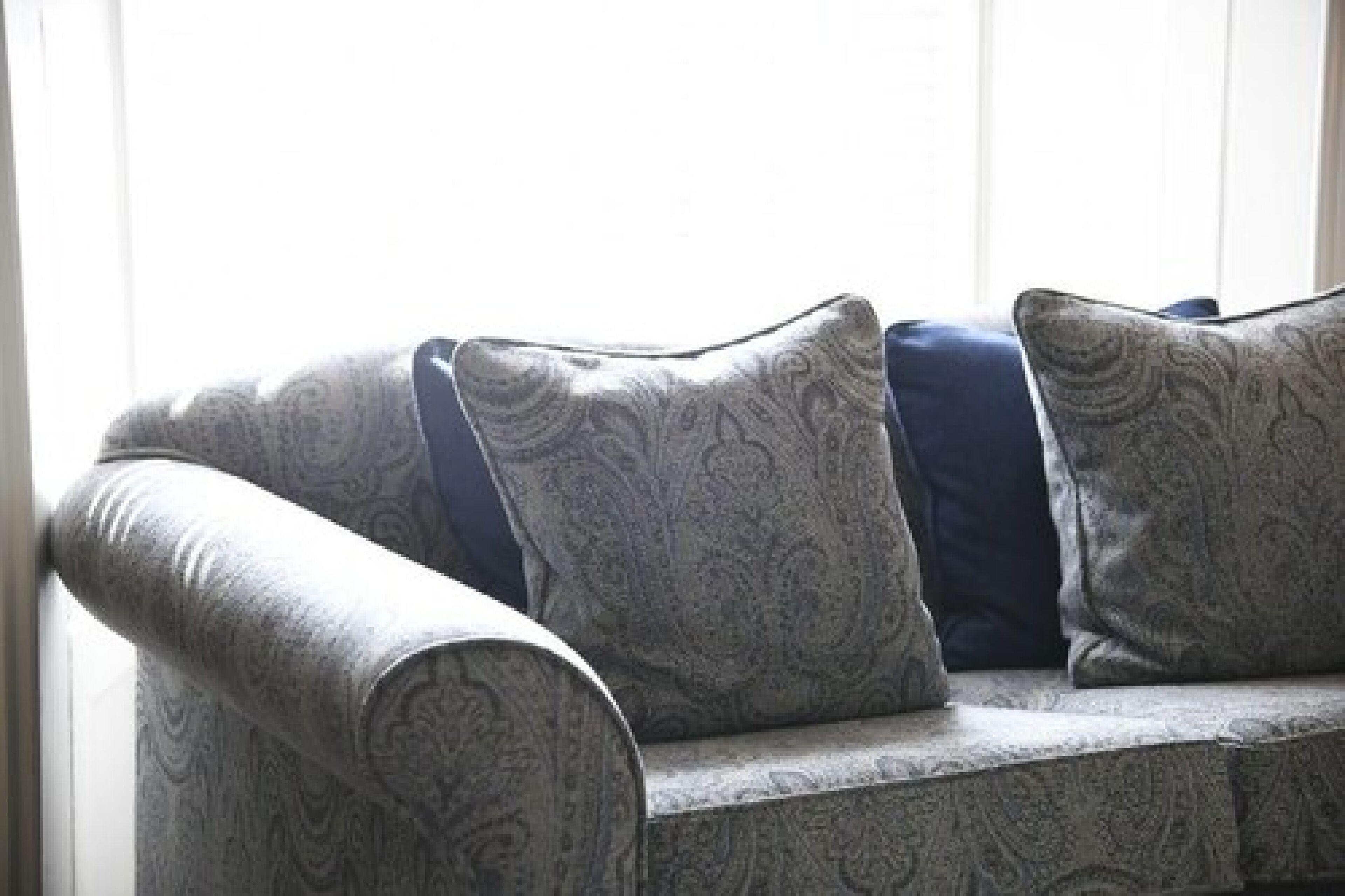 Un sofá de color gris con estampado, con cojines azules, en una habitación con un ventanal grande.