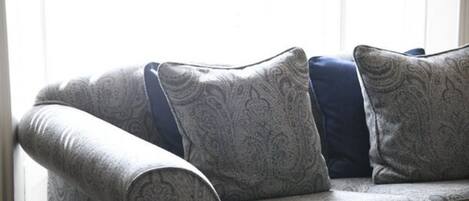 Un sofá de color gris con estampado, con cojines azules, en una habitación con un ventanal grande.