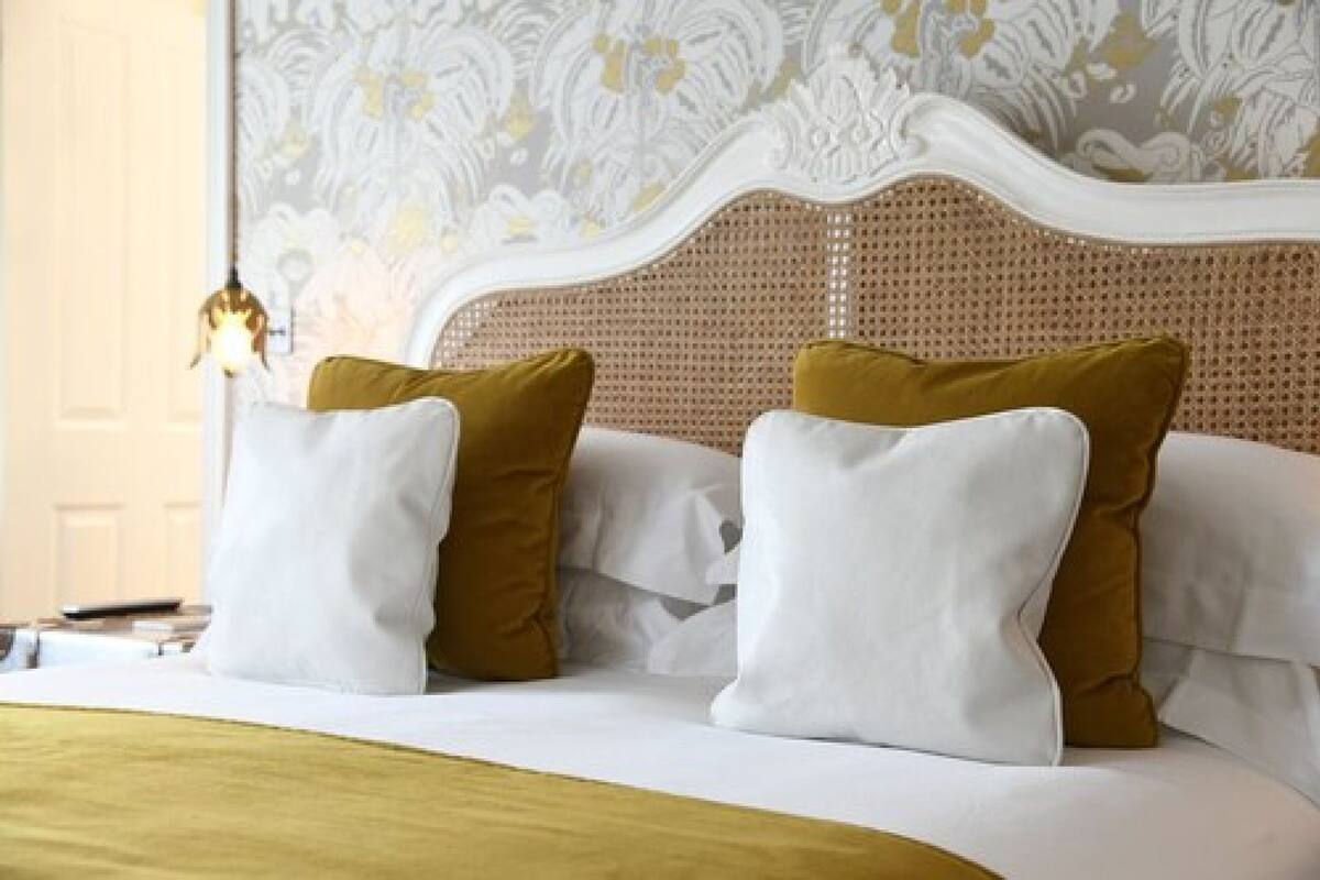 A bed with white and mustard pillows, a woven headboard, and a hanging light fixture.