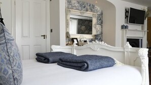 A bedroom with a white bed, two folded towels, a mirror, a television, and a fireplace. - Padstow Townhouse (Padstow)