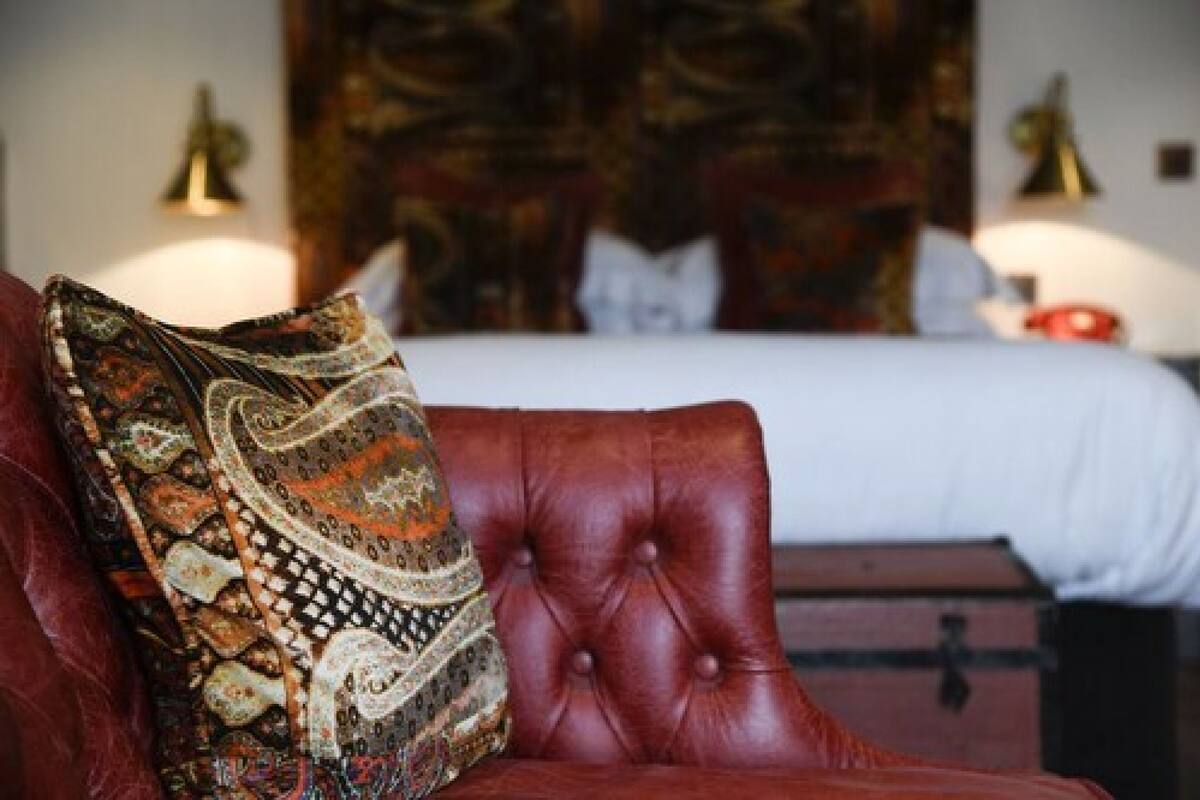 A red leather armchair with a patterned pillow, a bed with white bedding, and a headboard with a decorative design.