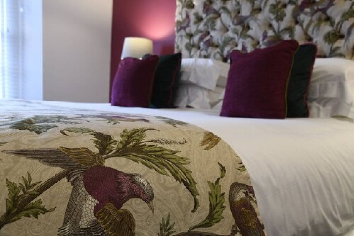 A bed with a floral headboard, a white pillow, and a red pillow.