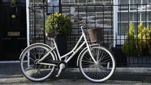 A white bicycle with a basket, parked in front of a stone building with a black door and a window. - Padstow Townhouse (Padstow)